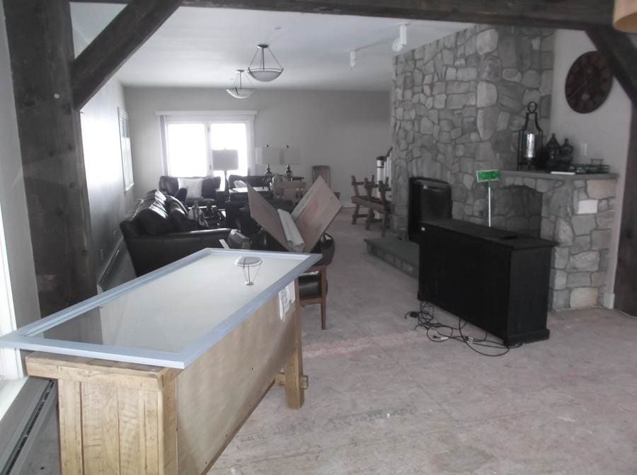 Living room mid-reconstruction with subfloor exposed and contents staged, stone fireplace wall